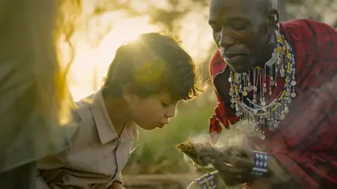 A Maasai guide and a young boy coaxing a bundle of tinder into flame