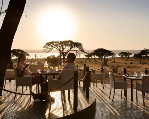 A couple at breakfast on a camp deck as the sun rises over the acacias