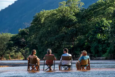 A family settled into camp chairs at the river's edge below forested hills