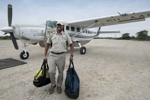 A guide carrying bags to a light aircraft waiting on a bush airstrip