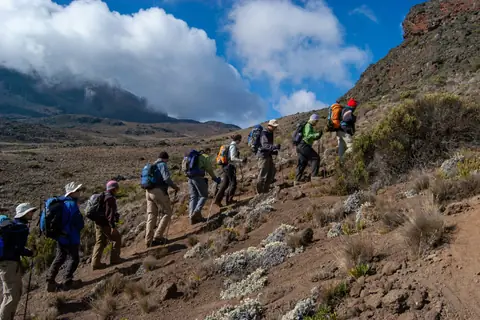 Trekkers strung out along a mountain path below cloud-covered slopes