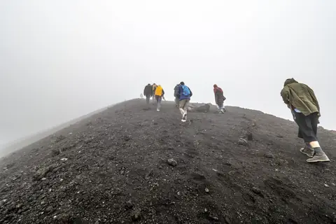 Walkers following a scree ridge through thick mountain mist