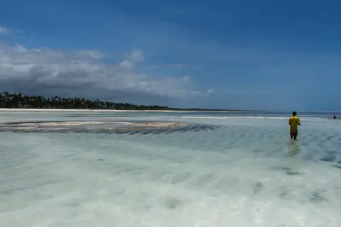 A figure wading the shallow flats off a Zanzibar sandbank