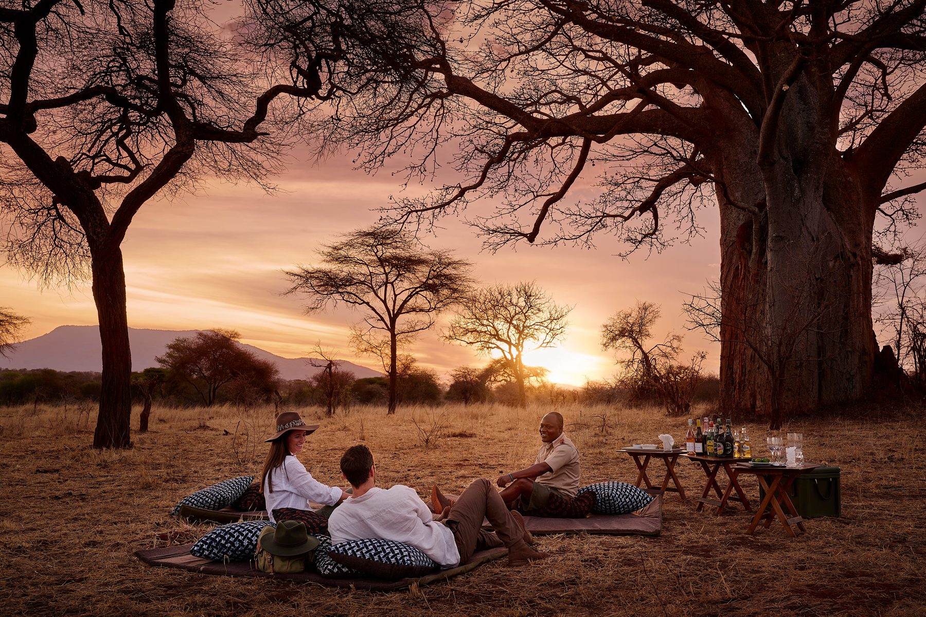 Guests gathered for sundowners beneath a baobab as the sun sets
