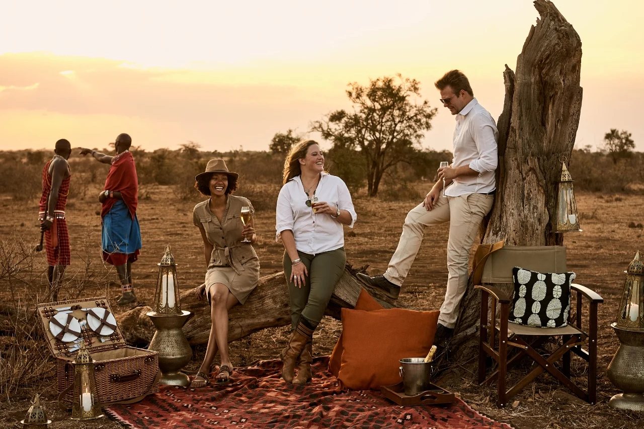 Guests and Maasai hosts gathered for a bush sundowner at dusk